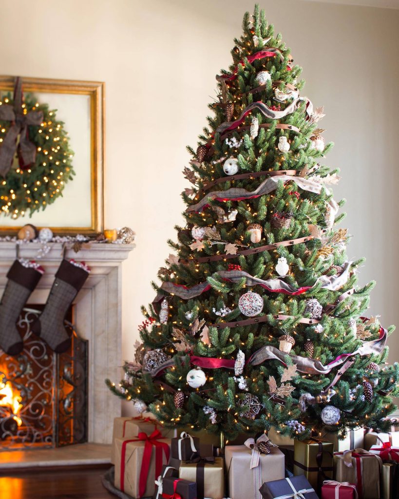 an elegnat christmas tree with ribbon garland and glass ornaments sits by a stone fireplace.