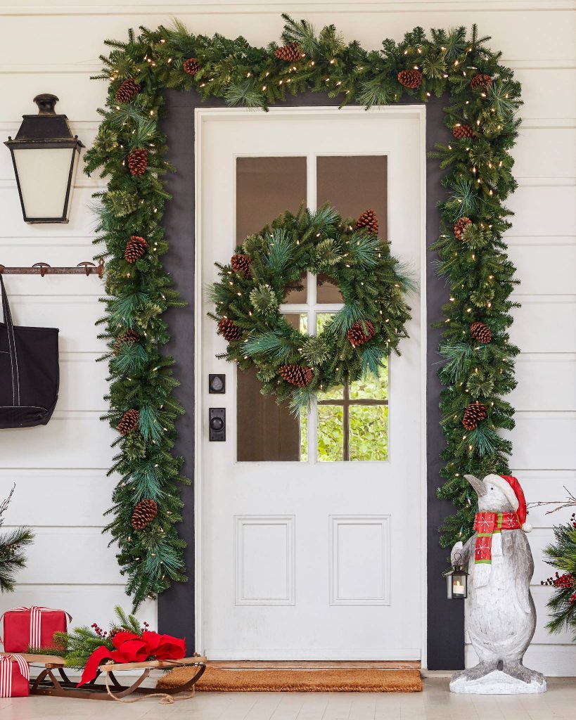 A white cottage front door with a pine garland and matching wreaths. 