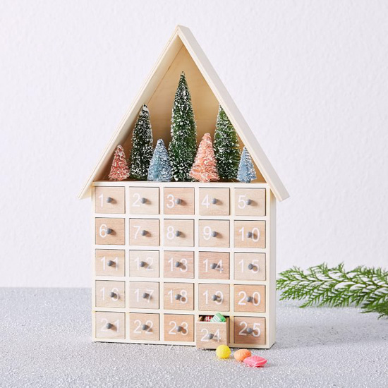 Light colored house shaped advent calendar with 25 pull out boxes and snowy, bottle brush trees at the top.