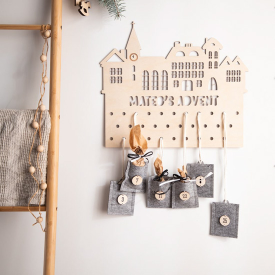 Personalized, laser cut, wooden advent calendar hanging on a white wall next to a decorative ladder.