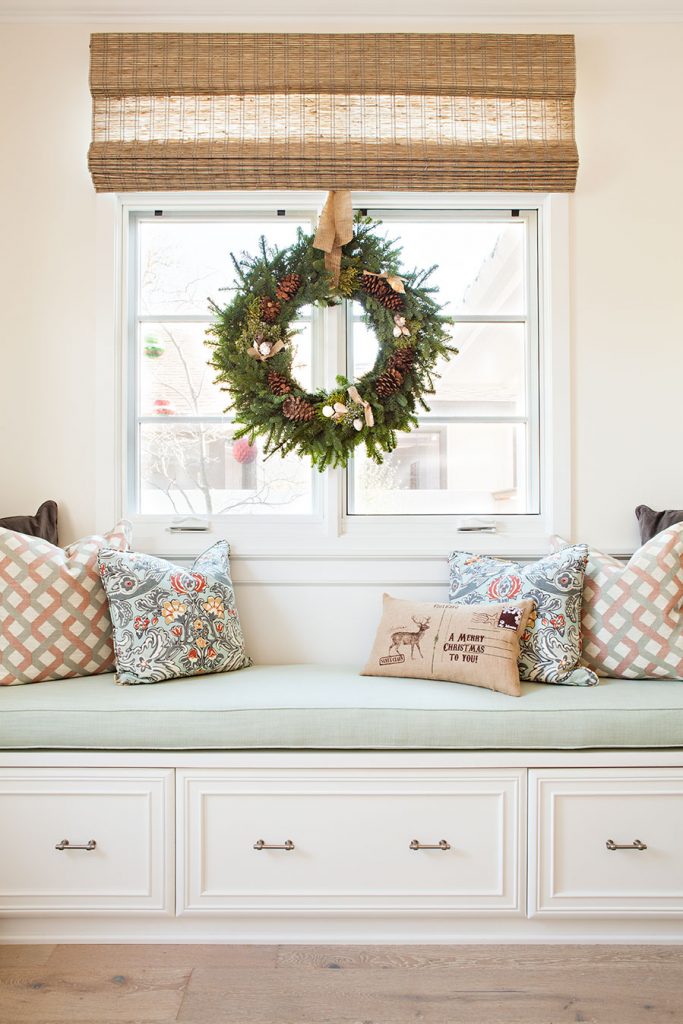 festive christmas wreath over a window above a built-in window seat.
