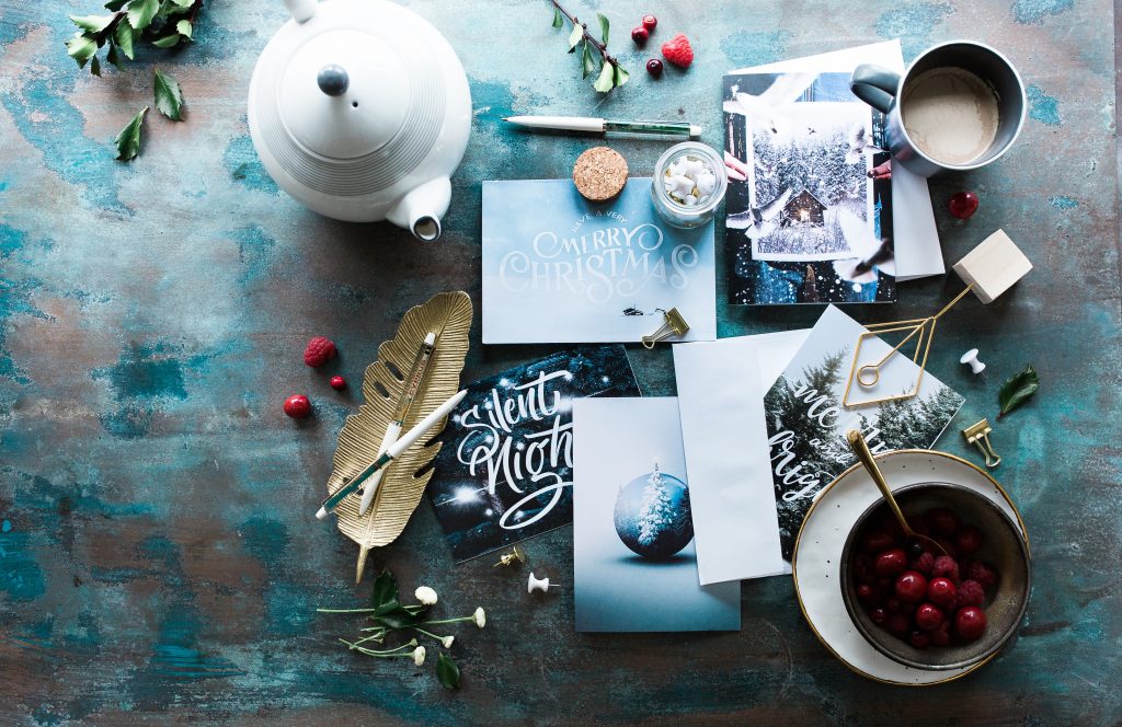 an arrangment of beautiful holiday cards on a blue painted tabletop surrounded by team, flowers and cranberries