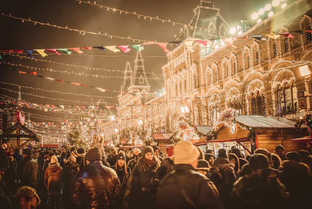 outdoor christmas market full of crowds and strings of lights hanging between small house shaped stalls. 