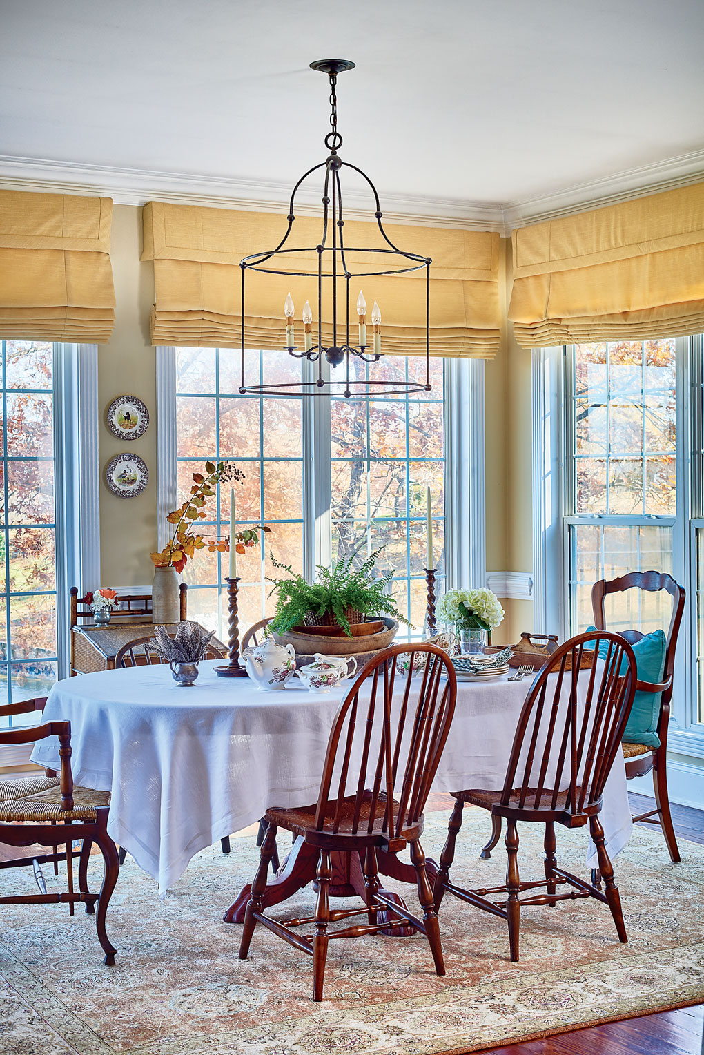 Breakfast nook surrounded by windows and a lake view with high back wooden chairs and light yellow walls and window coverings. 