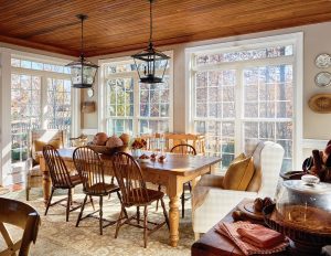 Lake house dining room with pine farm table and hanging lantern pendants overhead surrounded by a wall of windows.