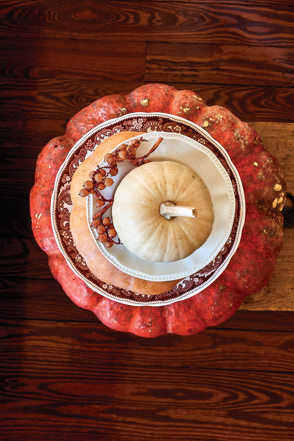 Aerial shot of a stack of layered pumpkins and fall themed china plates set on a wooden grain table. 