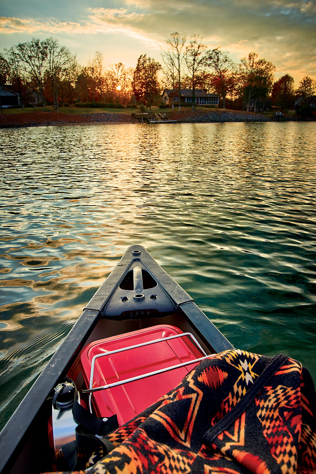 Private kayak cozied up with a blanket and cooler set out on a lake at sunset. 