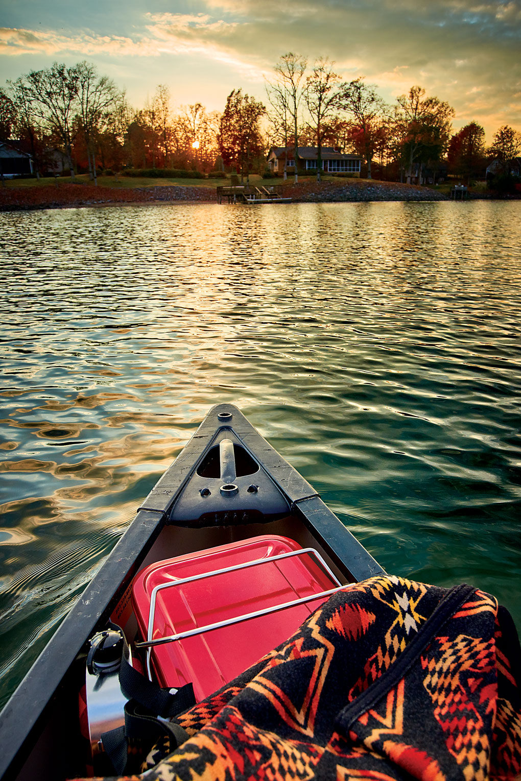 Private kayak cozied up with a blanket and cooler set out on a lake at sunset.