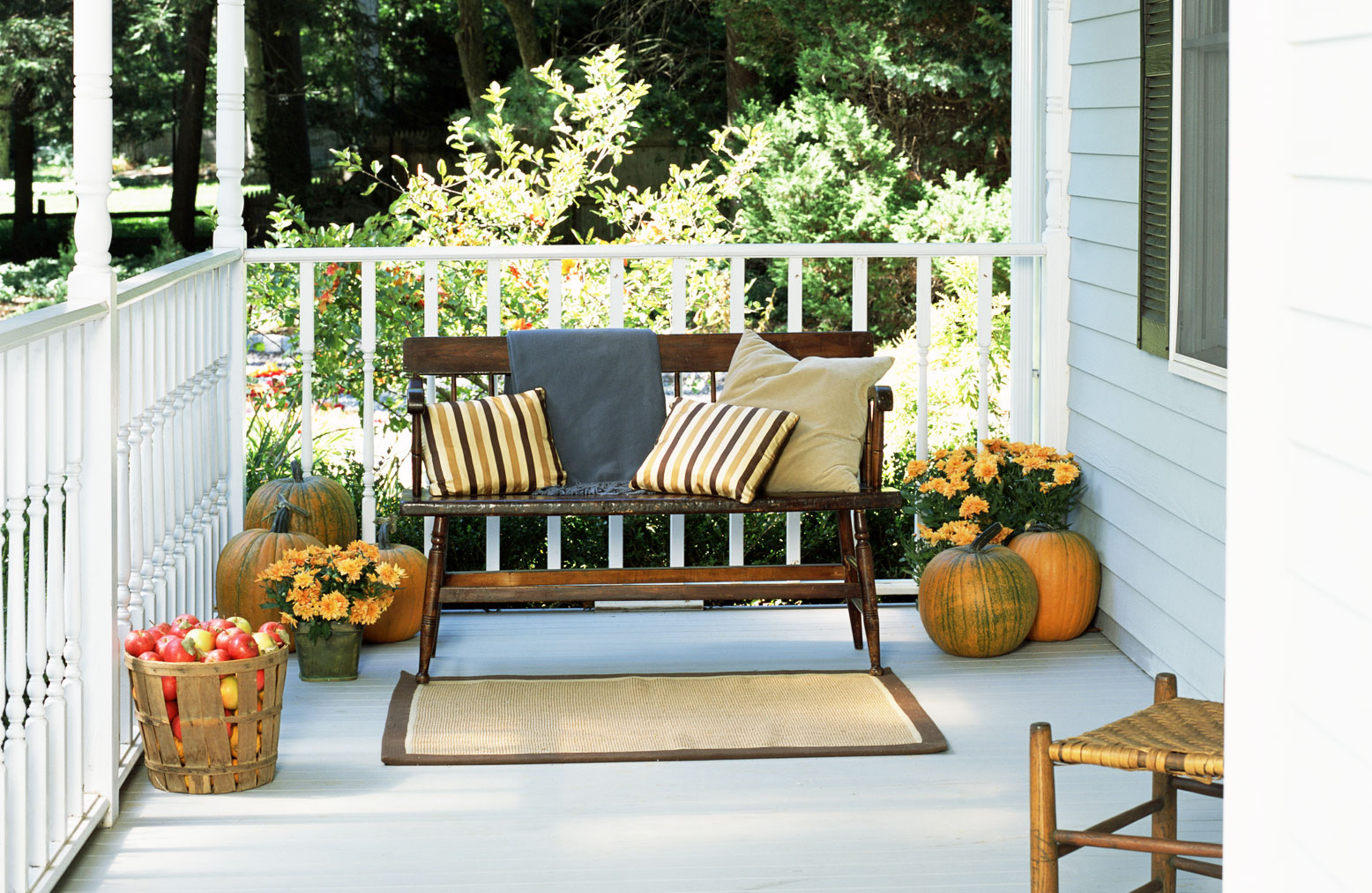 fall porch with vintage wooden bench, striped pillows in fall colors and pumpkins and apples in a basket