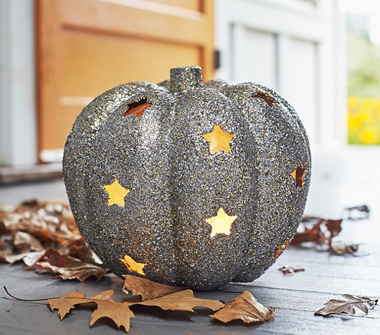 Silver glitter pumpkin with star cut-outs and light illuminating through the holes sitting on a front porch littered with fall leaves.