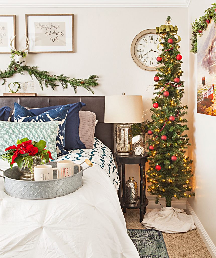 bedroom with a small christmas tree, fresh garland above the headboard and holiday flowers on a breakfast tray. 