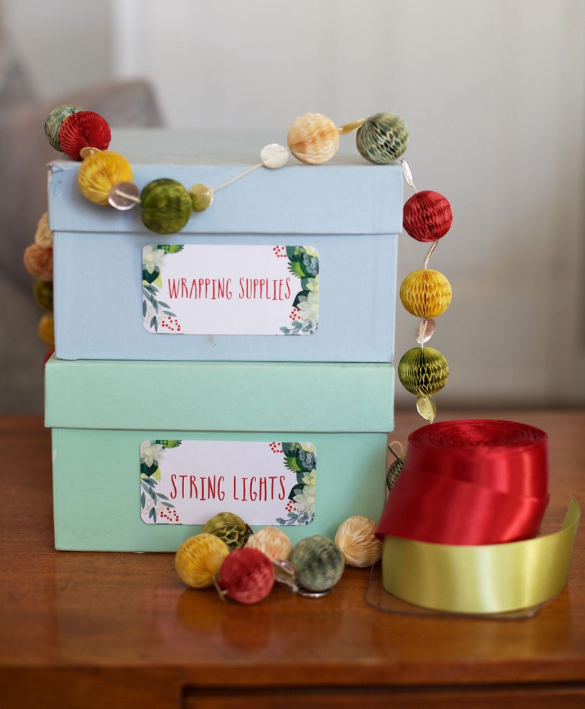 small lidded organiing boxes are labeled with festive holiday label stickers marked "wrapping supplies" and "Sting Lights"