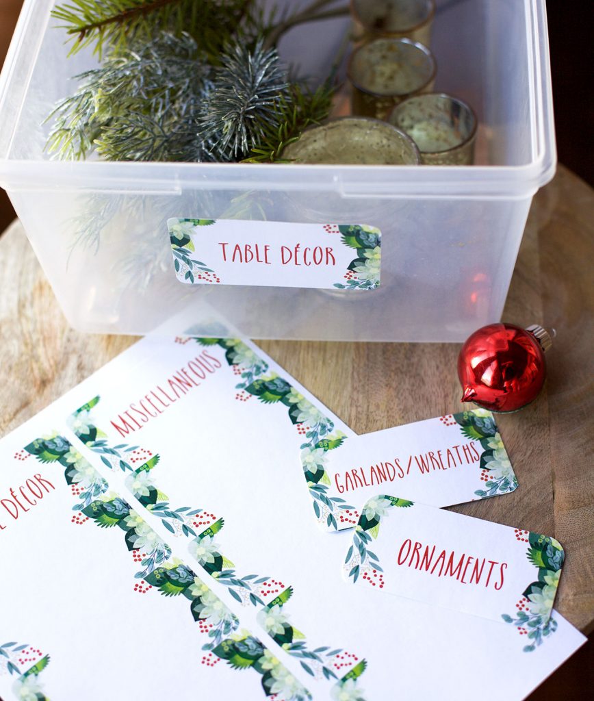clear tupperware box labeled "table decor." Inside are glass votives and artificial pine accents.