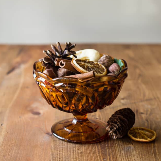 Amber colored glass bowl filled with homemade fall potpourri on a wooden table.