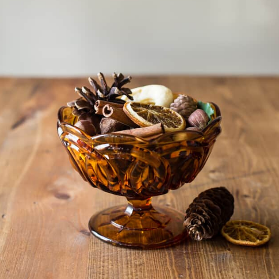 Amber colored glass bowl filled with homemade fall potpourri on a wooden table. 