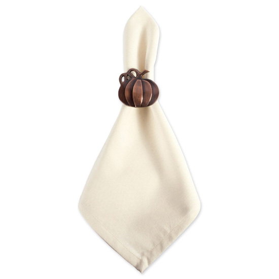 Cream colored cloth napkin with a brass pumpkin shaped napkin ring wrapped around it. 
