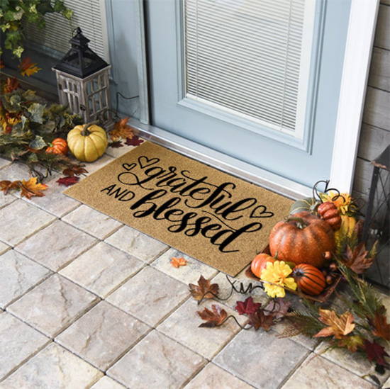 Jute front door mat that says "grateful & blessed" placed in front of a door surrounded by a lantern and fall decor.