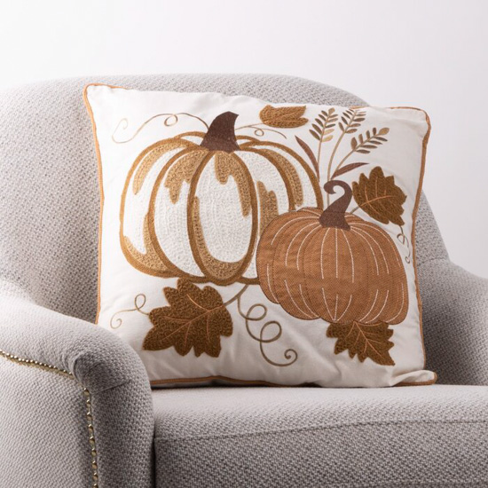 Oatmeal colored armchair with embroidered pumpkin throw pillow.