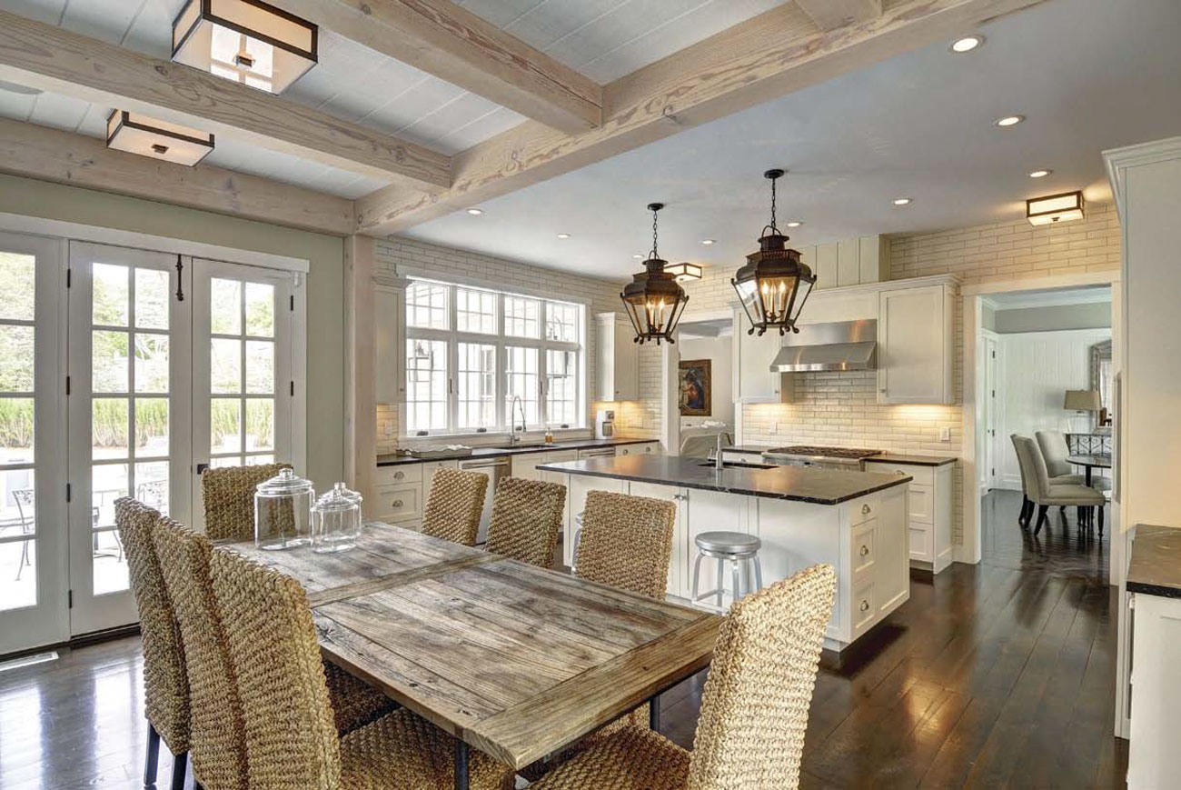 Expansive dining area and kitchen with exposed light colored beams and antique styled pendant lights hanging over the island.