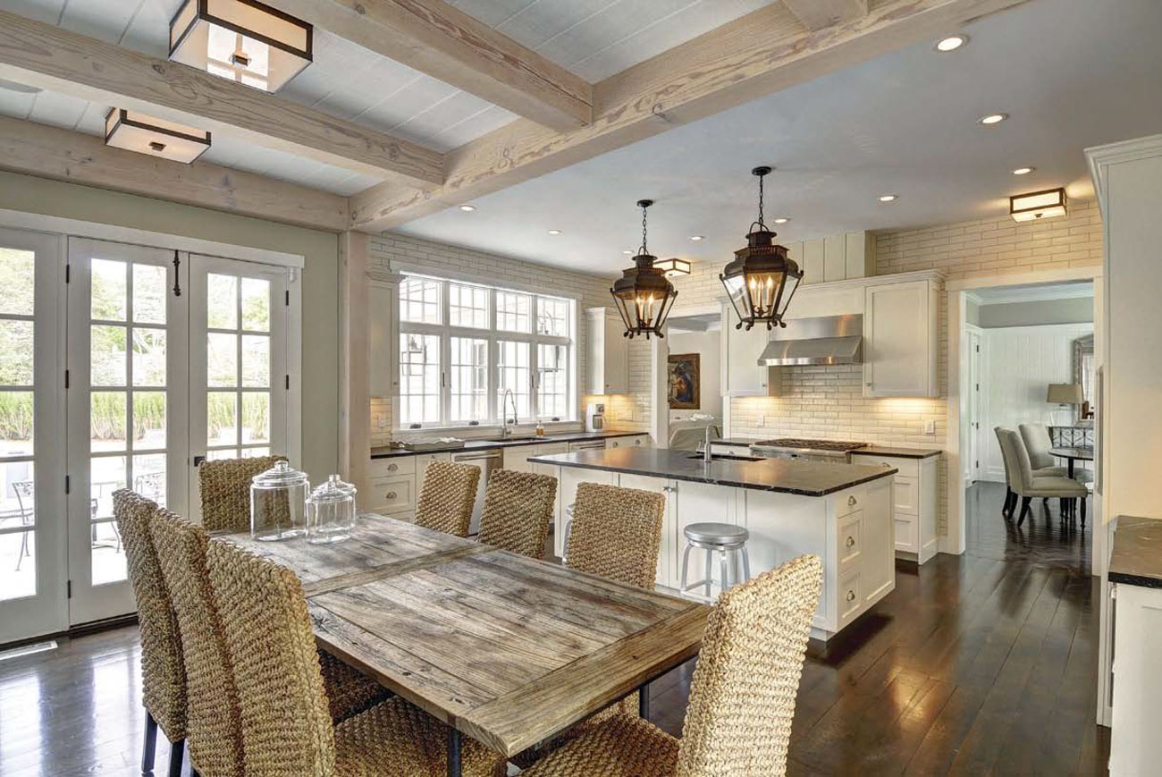 Expansive dining area and kitchen with exposed light colored beams and antique styled pendant lights hanging over the island. 