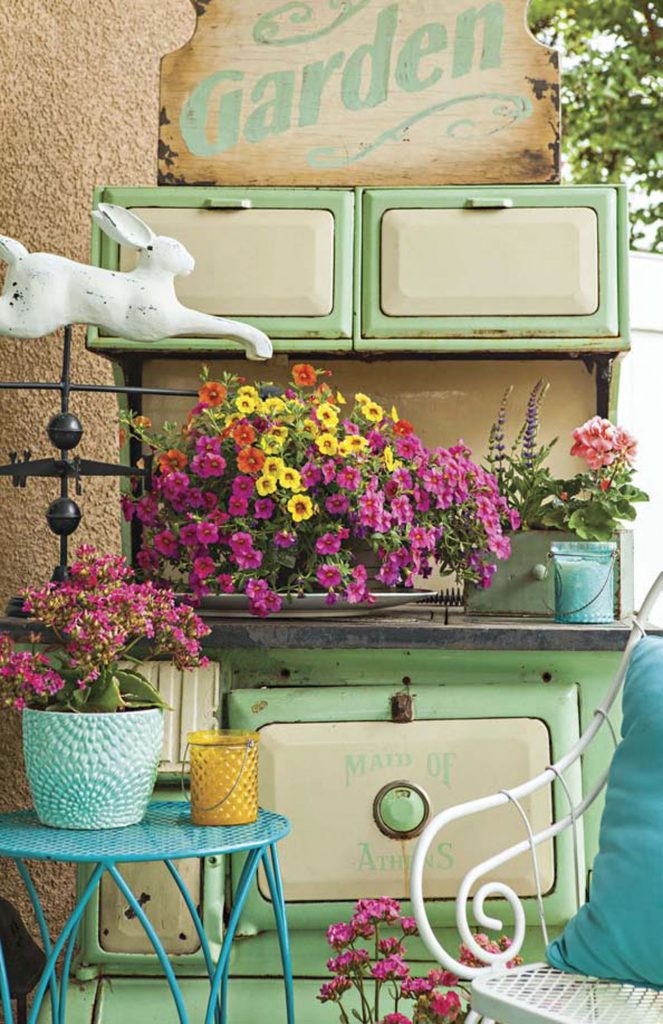 Back porch with a vintage mint green stove surrounded by flowers and an iron seating set. 