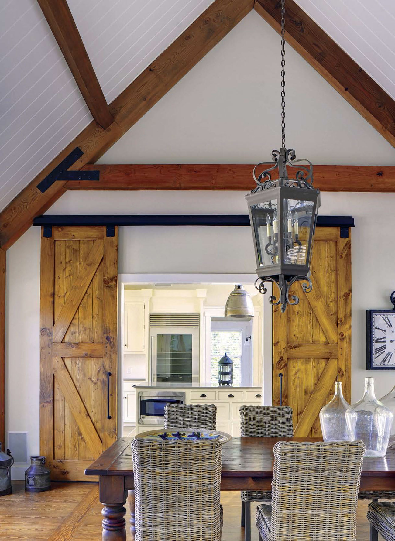 A pitched ceiling with exposed beams and a large lantern pendant hanging over the dining room with sliding barn doors that open to the kitchen.