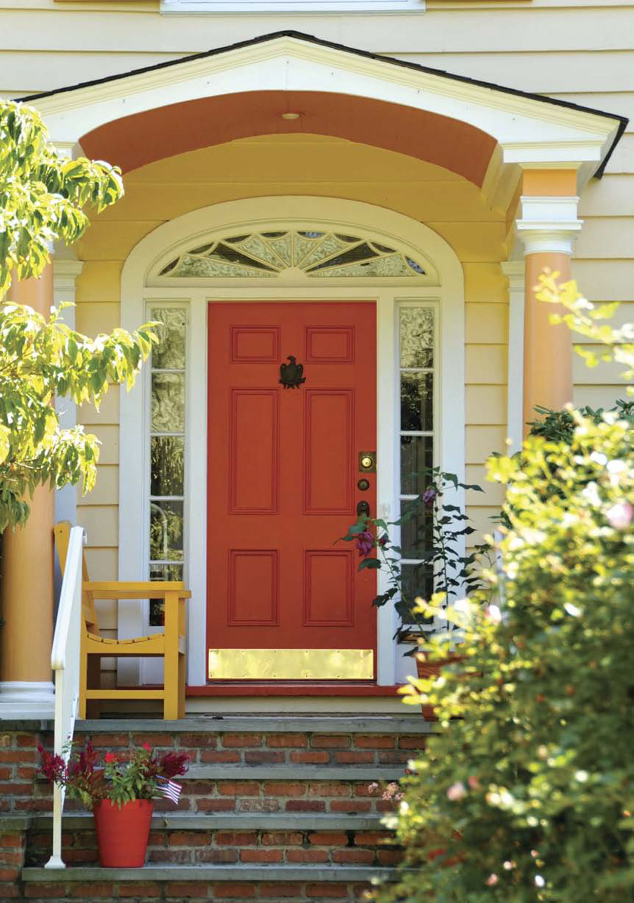 Brick front steps to a small porch with a red door surrounded by panes of glass. 