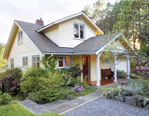 Outside view of a quaint light yellow cottage with blue trim.