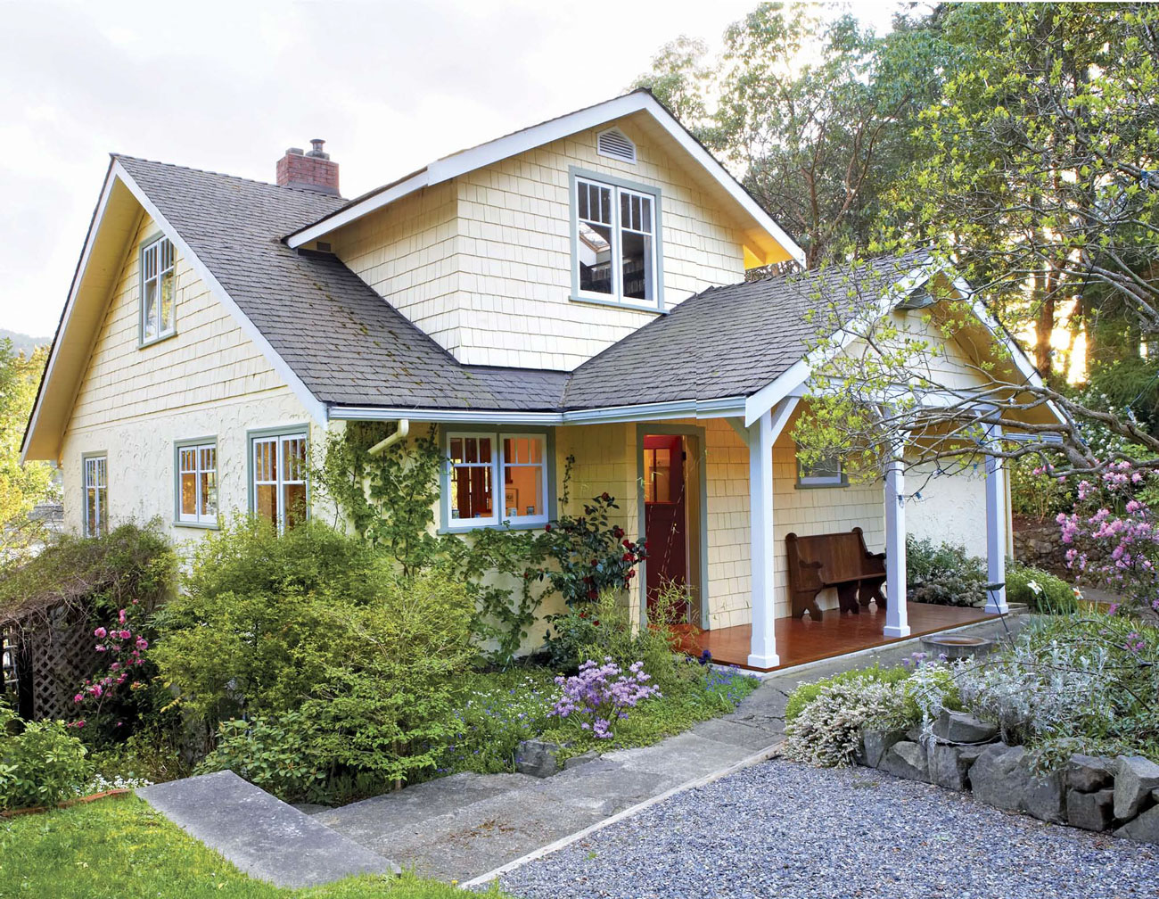 Outside view of a quaint light yellow cottage with blue trim. 