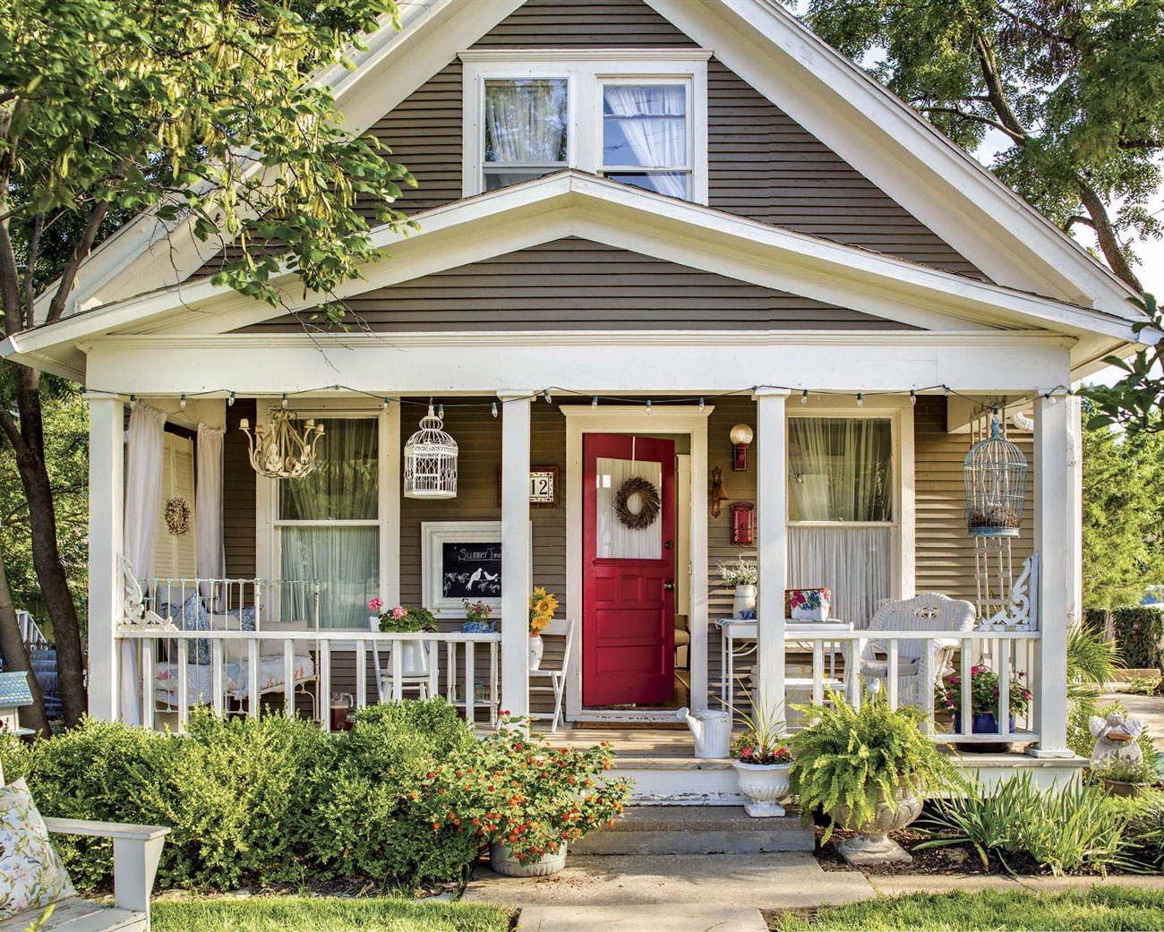 Home exterior view of a cottage with a cozy front porch and bright red door with a wreath. 