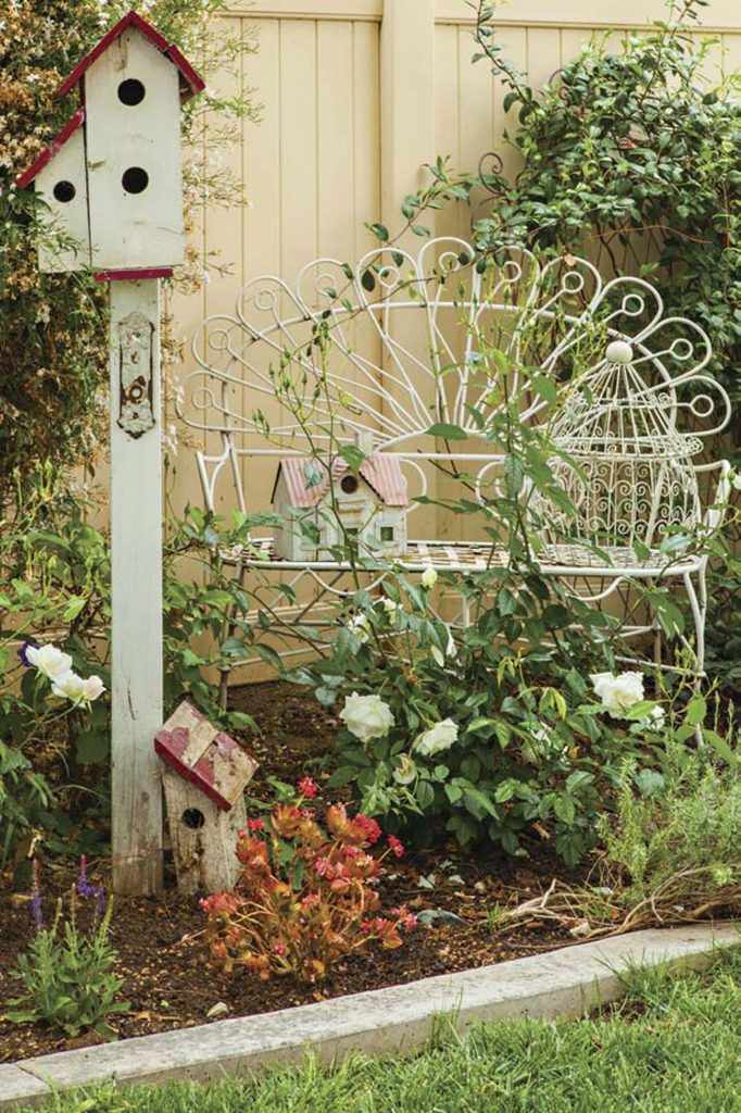 Wrought iron white peacock bench and rustic birdhouses in a garden.