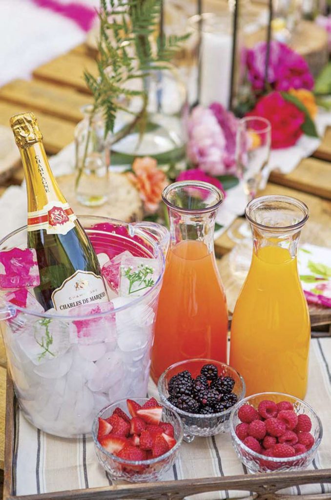 A bright and colorful mimosa bar with champagne on ice and fresh juices and fruit to garnish. 