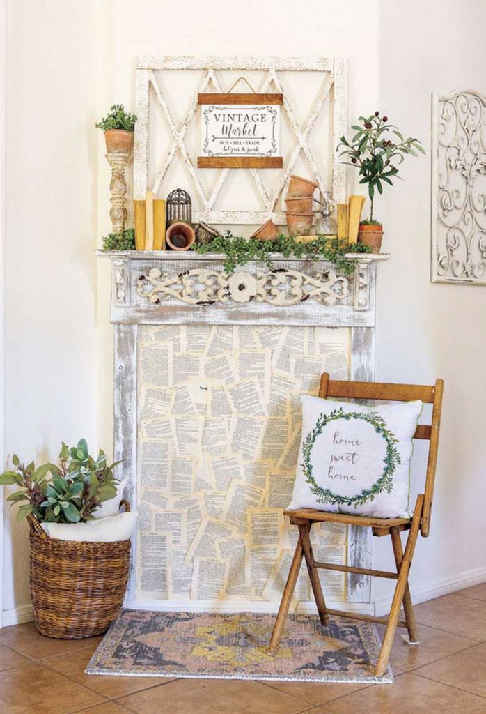 Rental style faux mantle filled with paper book pages next to a wooden folding chair and woven basket filled greenery. 