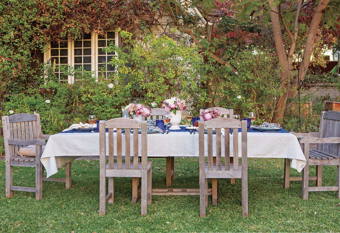 long table with 6 chairs, white and blue linens and floral arrangements in a garden 