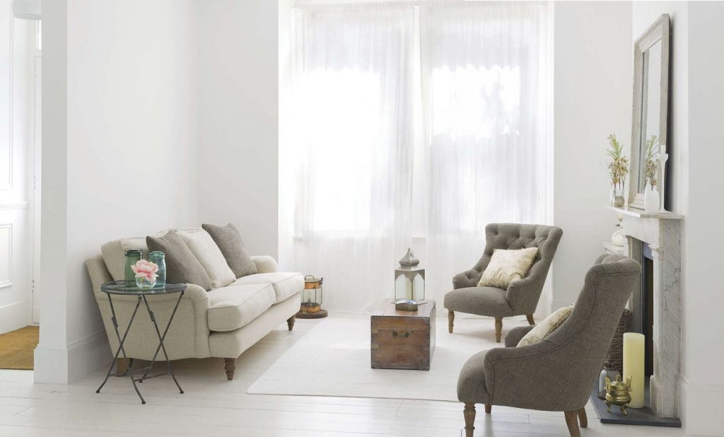 Bright white modern cottage living room with a natural colored couch and twin tufted gray chairs. 