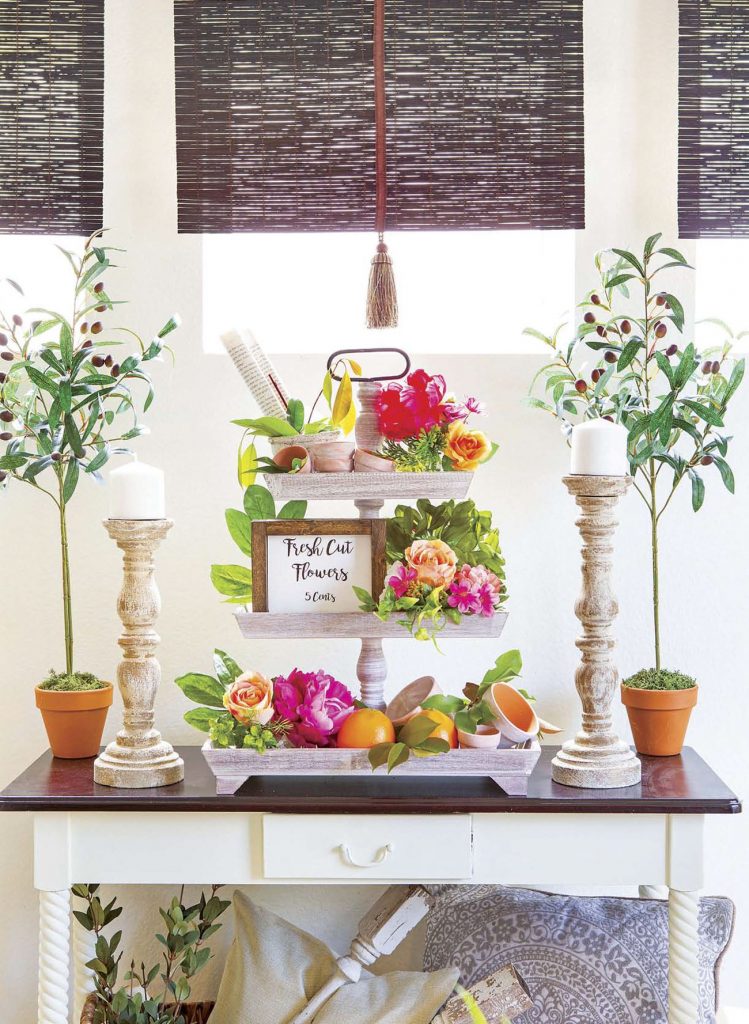 White entry table topped with faux greenery and tall candlesticks with a floral centerpiece. 