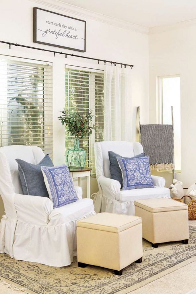 White draped armchairs with matching denim blue pillows and square cream colored ottomans. 