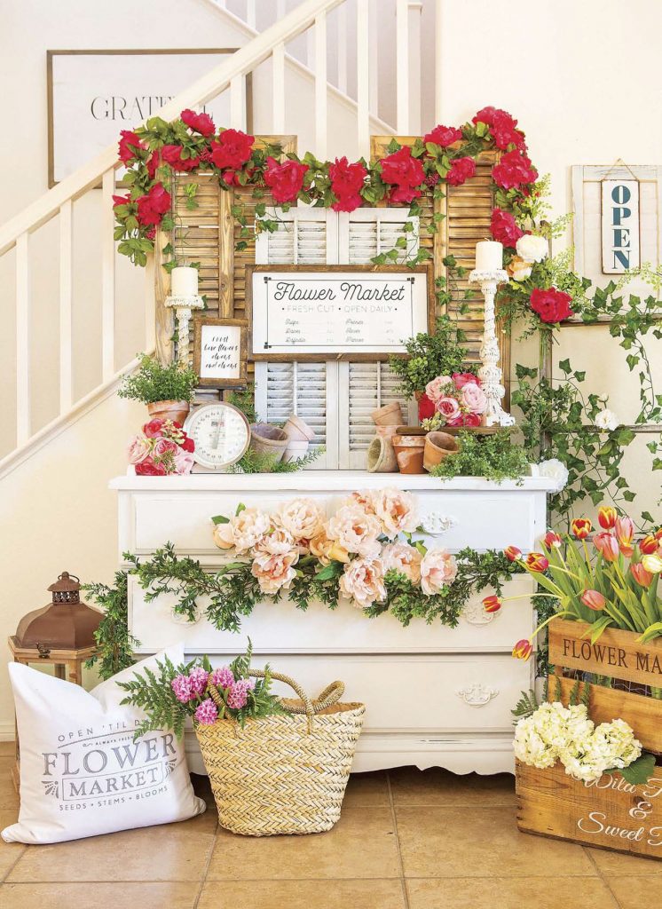 Faux flower market made up of a white dresser and shutters and a copious amount of fresh flowers. 