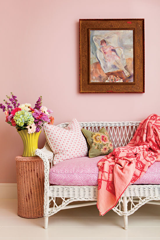 Pink bedding and a pink statement wall with vintage art hanging on the wall and a white whicker daybed. 