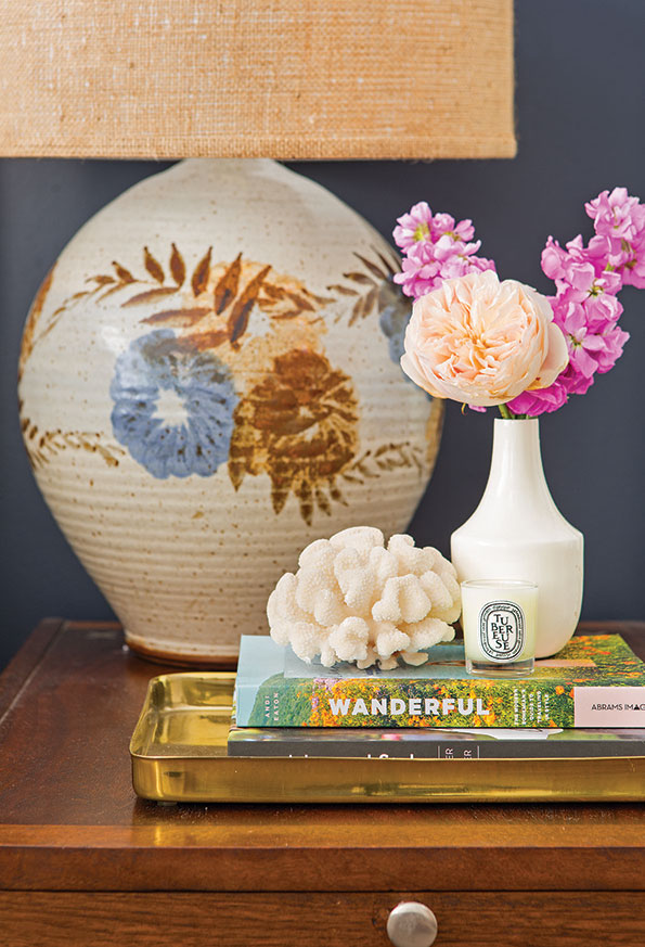 Mid-century side table topped with a mix of vintage and new decor with fresh flowers and vintage lamp. 