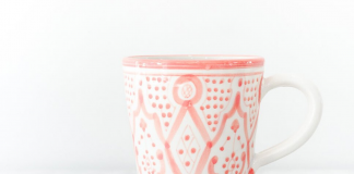 Ceramic white mug with pink designs wrapped around it sitting on a marble countertop next to sugar cubes.