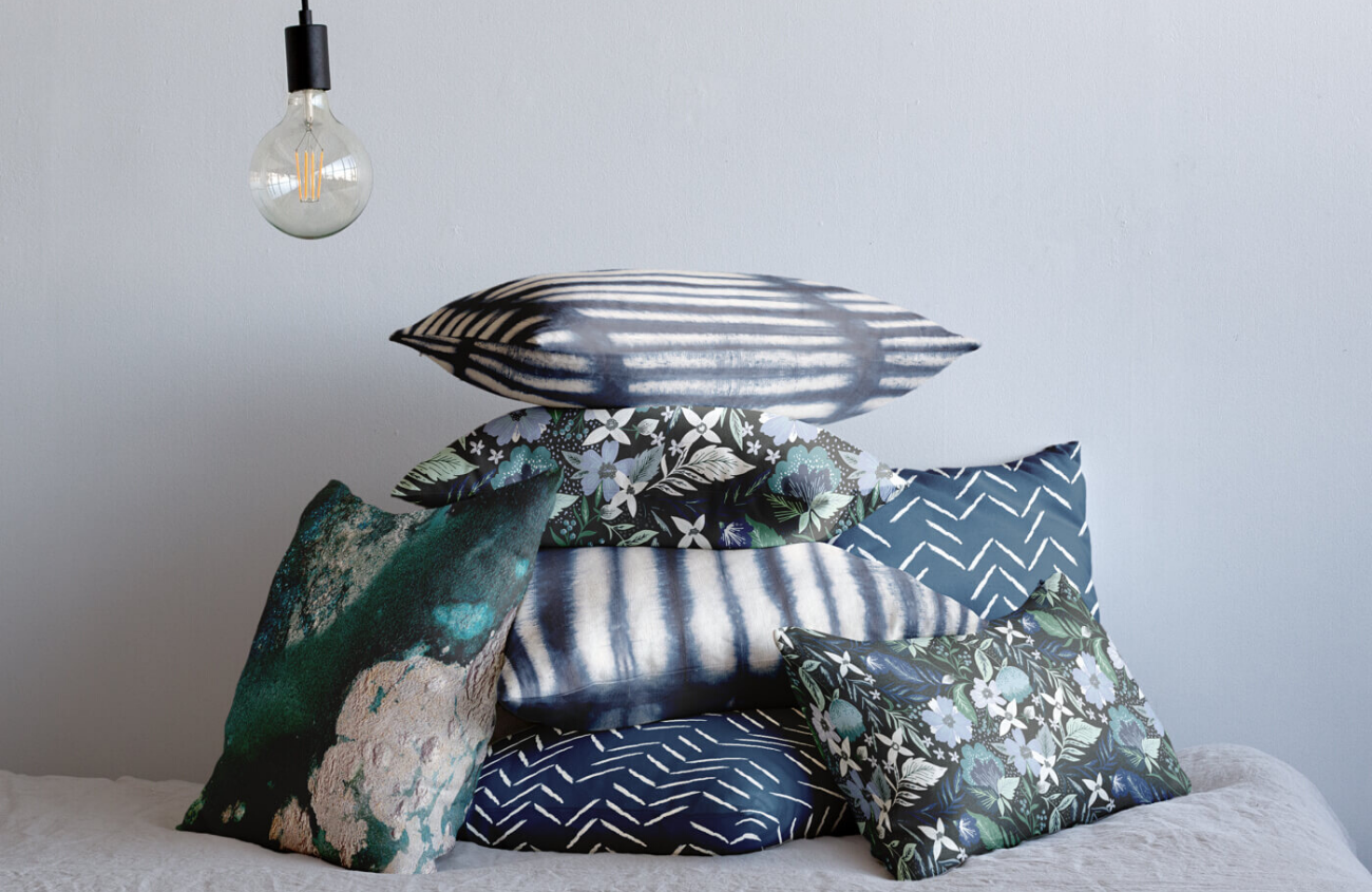 Pile of throw pillows in various blue prints with a modern light hanging into the frame.