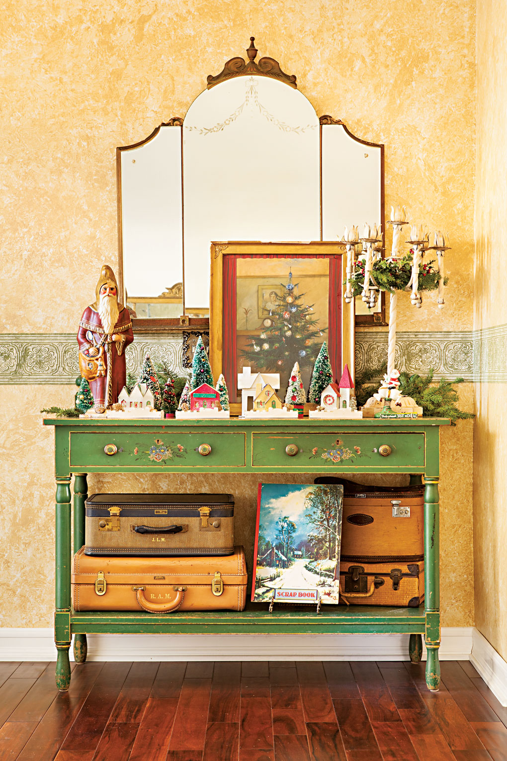 A vintage green entryway table adorned with a village of bottlebrush trees and putz houses next to an elegant candelabra. 