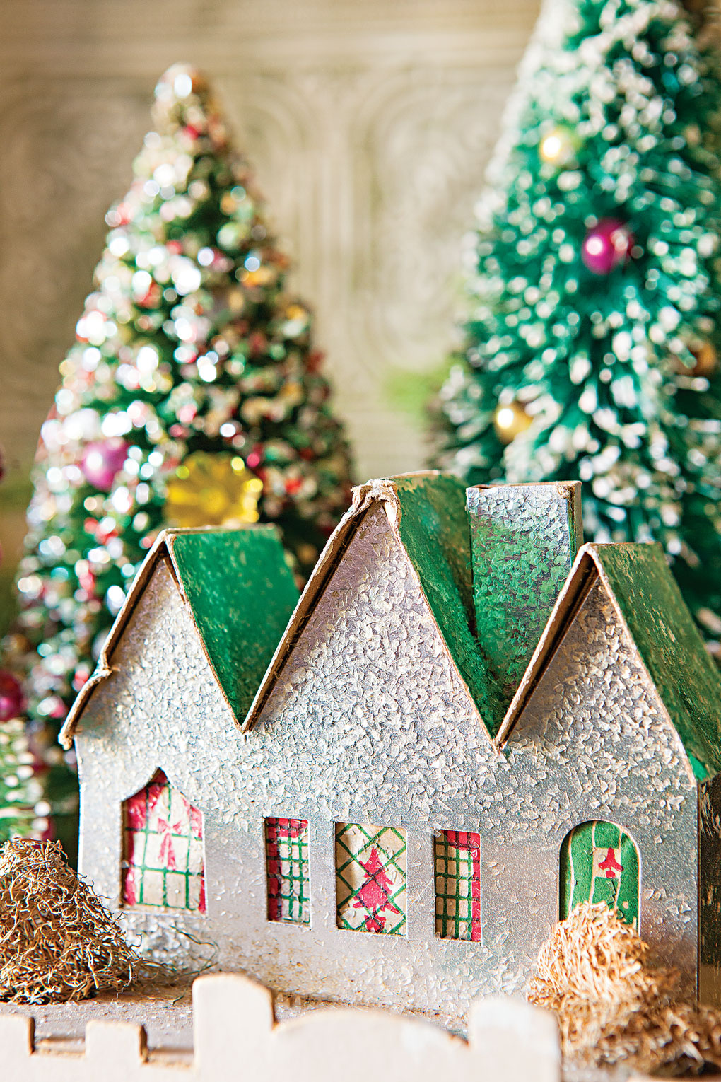 Vintage Christmas cottage display in front of charmingly decorated bottle brush trees.