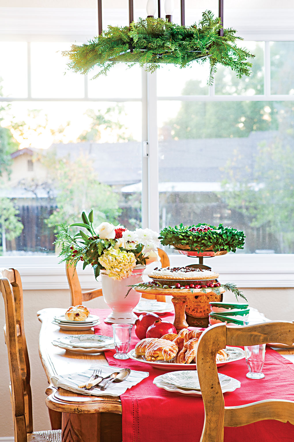 Wooden table and chairs set up for a holiday feast complete with a red table runner and bright colored Christmas accents. 