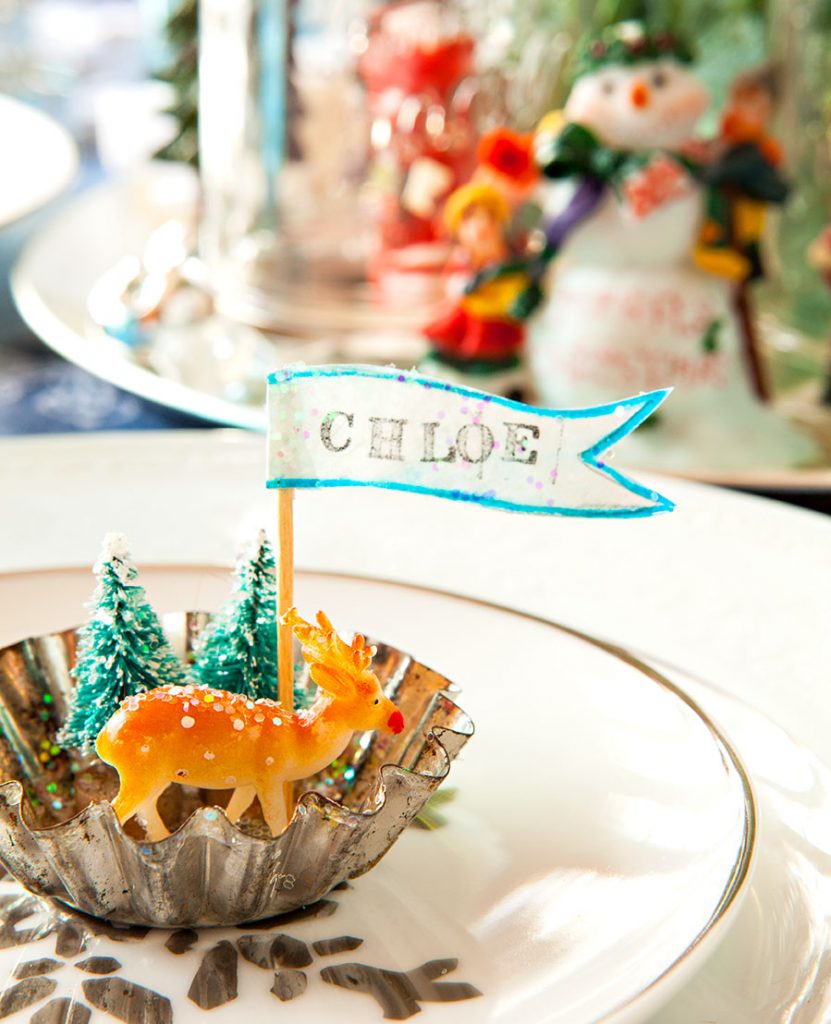 A place setting created by gluing trees, a deer and a name flag to the base. 