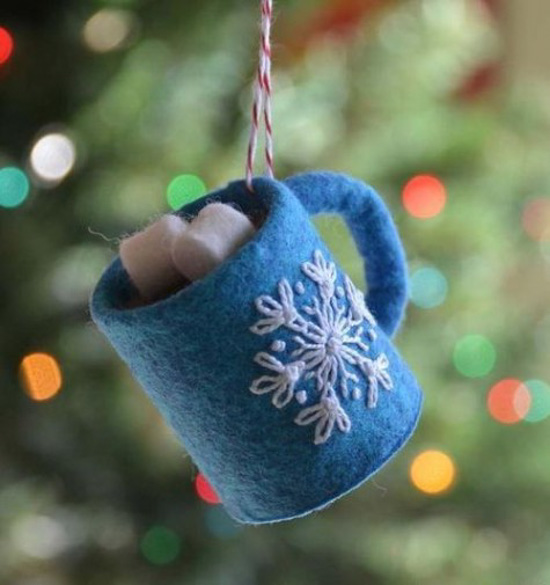 Homemade ornament that looks like a blue mug filled with cocoa and marshmallows hanging from a Christmas tree. 