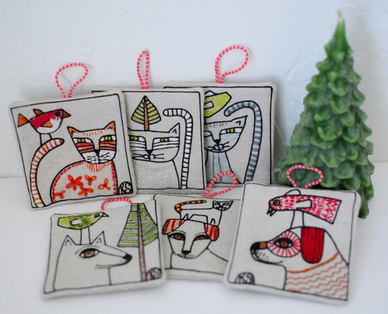 Set of 6 square embroidered ornaments with cats and dogs on the front next to a small wax candle tree. 