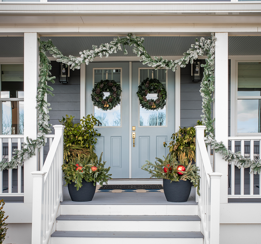 front farmhouse style porch with flocked pine swap and a two robins egg blue doors each with their own wreath
