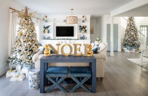 living room with white shiplap walls, a large flocked christmas tree and a blue hall table with blue x-bench stools underneath